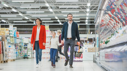 At the Supermarket: Happy Family of Three, Holding Hands, Walks Through Fresh Produce Section of...