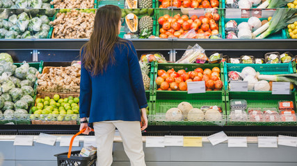 At the Supermarket: Woman Chooses Organic Fruits in the Fresh Produce Section of the Store. She is Looking for Cantaloupe. Holding Shopping Basket. Back View Shot.