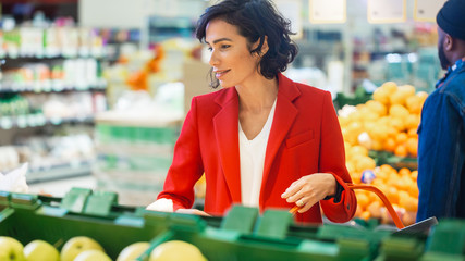At the Supermarket: Portrait of the Beautiful Smiling Woman Choosing Organic Fruits In the Fresh Produce Aisle and Puts them into Shopping Basket.