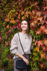 Stylish young woman wearing beige sweater and coat outdoors. Female model in trendy outfit on the steet wall background