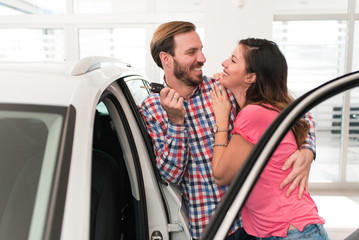 Young beautiful happy couple buying a car together and smiling. Couple in car showroom, salon looking for cars to buy.