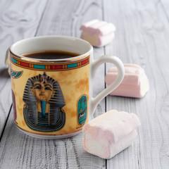 A Cup of coffee with Egyptian patterns and sweet marshmallows on a light wooden background