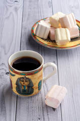 A Cup of coffee with Egyptian patterns and sweet marshmallows on a light wooden background