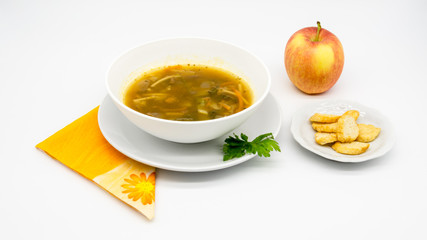 A delicious soup dish with pasta, toasted bread, vegetables and an apple beside it, decorated with parsley, over a orange napkin and with a large and clean white background