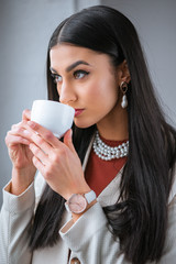 elegant young woman drinking coffee and looking away