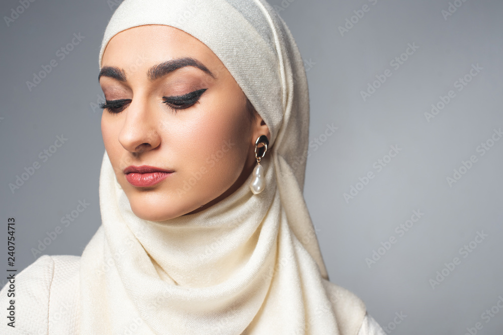 Wall mural close-up portrait of beautiful young muslim woman looking down isolated on grey