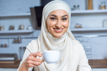 beautiful happy young muslim woman holding cup of coffee and smiling at camera