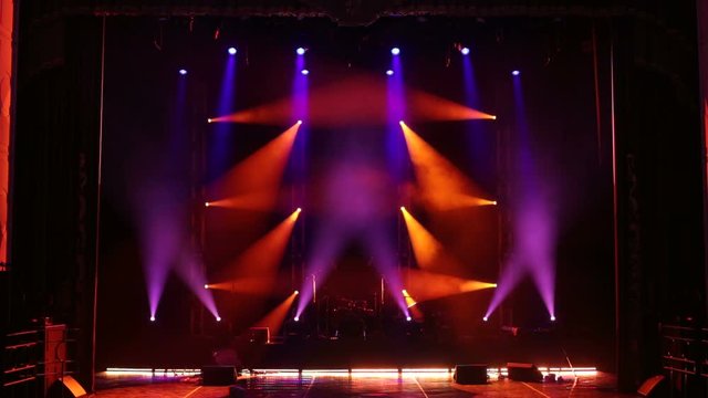 Multicolored rays on an empty stage in the dark. Stage lighting. Light show. Different color spotlights on empty stage with musical instruments and drum set.