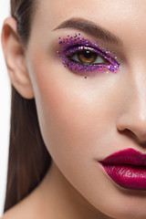 Close-up of the beauty of half a woman's face with creative fashionable make-up of sparkles. Black eyeliner and long eyelashes decorate hazel eyes and lips to match. Well-groomed skin after spa