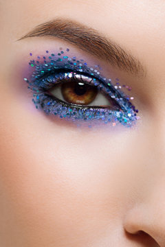 Close eye with colorful eyeshadow. Macro shot of opened female eye. Woman with evening beauty makeup. Girl with perfect skin and eyebrow. Women cosmetics, extremely long eyelash and ligth blue glitter