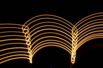 Light painting, long exposure photography, metallic yellow gold color loops and swirls of parallel lines against a black background