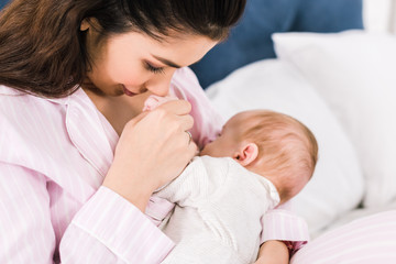 portrait of young mother breastfeeding little baby on bed at home