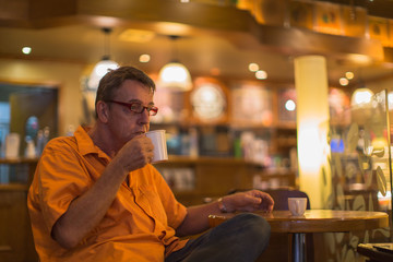 Man holding mug of coffee with a smile enjoying life in a Cafe wearing a orange shirt