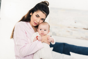 portrait of young beautiful mother with little baby on hands at home
