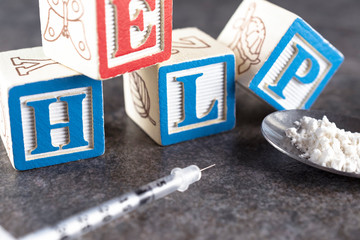 Help in jumbled blocks in the background with a syringe and a spoon filled with a white powder...