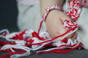 Martenitsa, white and red strains of yarn, Bulgarian folklore tradition, welcoming the spring in March, adornment symbol, wish for good health. Baba Marta Day. Cute baby toddler hand holding bracelets