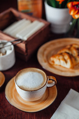 A cup of morning cappuccino and freshly baked pecans on a plate of warm flowers on a dark wood table