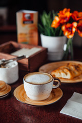 A cup of morning cappuccino and freshly baked pecans on a plate of warm flowers on a dark wood table