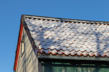Snow on the red roof of a house in winter under blue sky