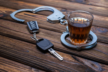 alcohol, handcuffs, car keys on wooden table background. driving under the influence. detention of...