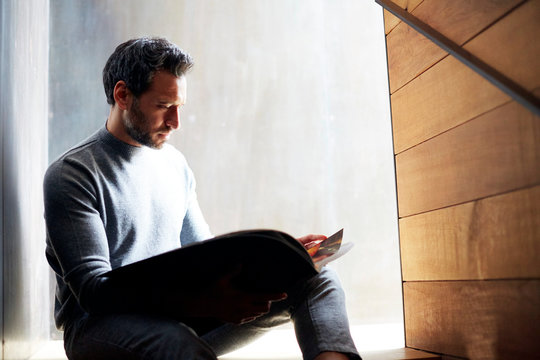 Junger Mann sitz auf Treppe vor Metall und Holz Wand und liest in Zeitschrift