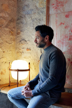 Junger Mann sitz am Fenster vor Steinwand und Lampe