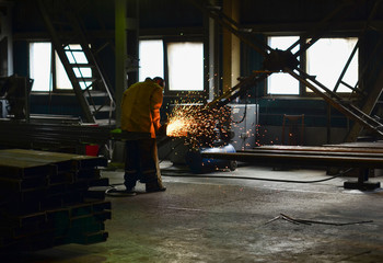 Fototapeta premium Industrial worker at an automotive plant for the production of pit dumpers and bulldozers, welding iron of an automotive part, close-up. Workflow at a heavy metal welding factory. Sparks fly