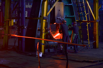 Hot metal ingot being loaded into a hammer forge. Worker forges iron products. Hot iron in smeltery held by a worker. High precision hot forging product, automotive part production by hot forging proc