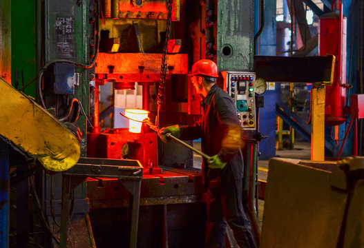 Hot metal ingot being loaded into a hammer forge. Worker forges iron products