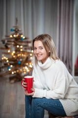 Young girl wearing a white sweater posing with a Christmas Tree