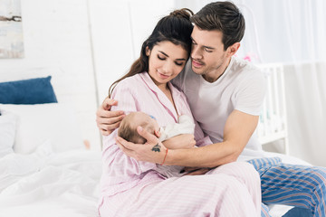 young man hugging wife with little son on hands at home