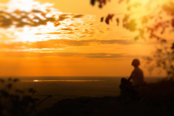 A lonely woman sits on the rock and enjoys the sunset