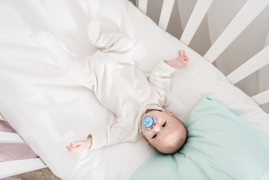 Overhead View Of Little Baby With Pacifier Lying In Crib