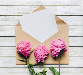 Valentine's Day concept. Three faded purple peonies and an open kraft envelope containing a white sheet of paper. Copy space, top view.