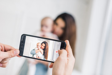 cropped shot of man taking picture of wife with baby in hands on smartphone