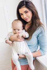 portrait of beautiful young mother holding little son in hands at home
