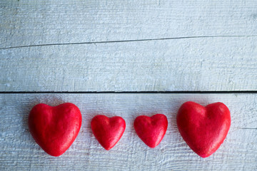 four red hearts of different sizes lie on a light wooden background. Love, family and Valentine's day