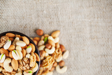 Mix of different nuts in a wooden cup against the background of fabric from burlap. Nuts as structure and background, macro. Top view.