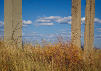 Fototapeta premium Concrete pillars. Yellow grass. Blue sky. Steppe. Abstract landscape