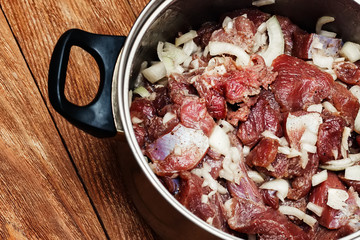 Marinated meat pieces with onions in pan on wooden background. Preparation of raw meat for barbecue. The view from the top. Raw beef mixed with onions and spices.