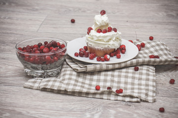 On a light tabletop on a linen napkin in a saucer cake with whipped cream with fresh berries, a bowl with red berries.