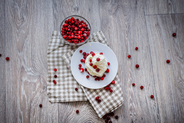 On a light tabletop on a linen napkin in a saucer cake with whipped cream with fresh berries, a bowl with red berries.