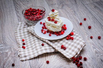 Obraz na płótnie Canvas On a light tabletop on a linen napkin in a saucer cake with whipped cream with fresh berries, a bowl with red berries.