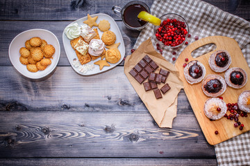 Happy New Year  cranberries, sweets in a dessert plate, a broken chocolate bar on kraft paper and a glass of tea with lemon on a linen napkin on a dark gray background.