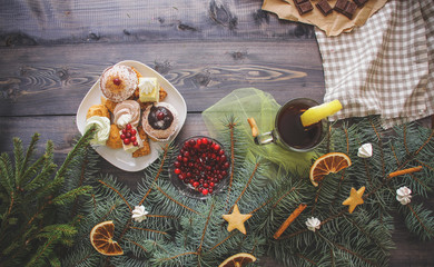 fir branches decorated with gingerbread stars, cinnamon sticks, dried orange slices and meringue peaks, bright cranberries, sweets in a dessert plate, a broken chocolate bar on kraft