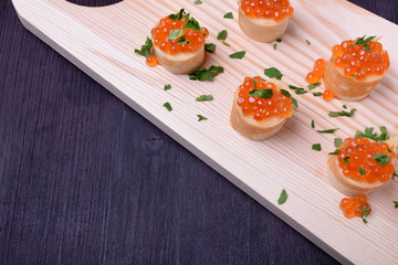 Crepes with red caviar on a wooden board sprinkled with parsley. Russian cuisine