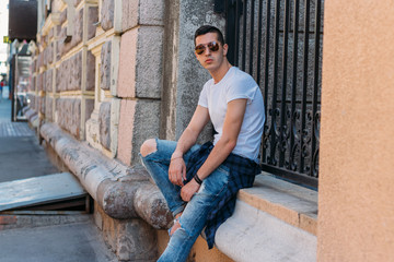 Attractive, sexy guy sits on the street in sunglasses. self-confidence, flatulence and arrogance. model, posing, portrait of a young man