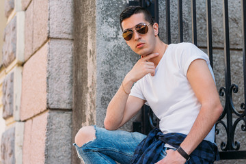 Attractive, sexy guy sits on the street in sunglasses. self-confidence, flatulence and arrogance. model, posing, portrait of a young man