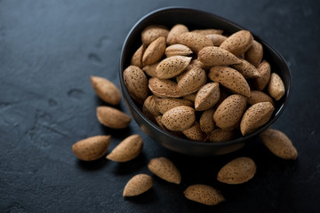 Bowl of unpeeled almonds on a black stone background, horizontal shot with space