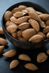 Close-up of unpeeled almond nuts in a black bowl, selective focus, vertical shot